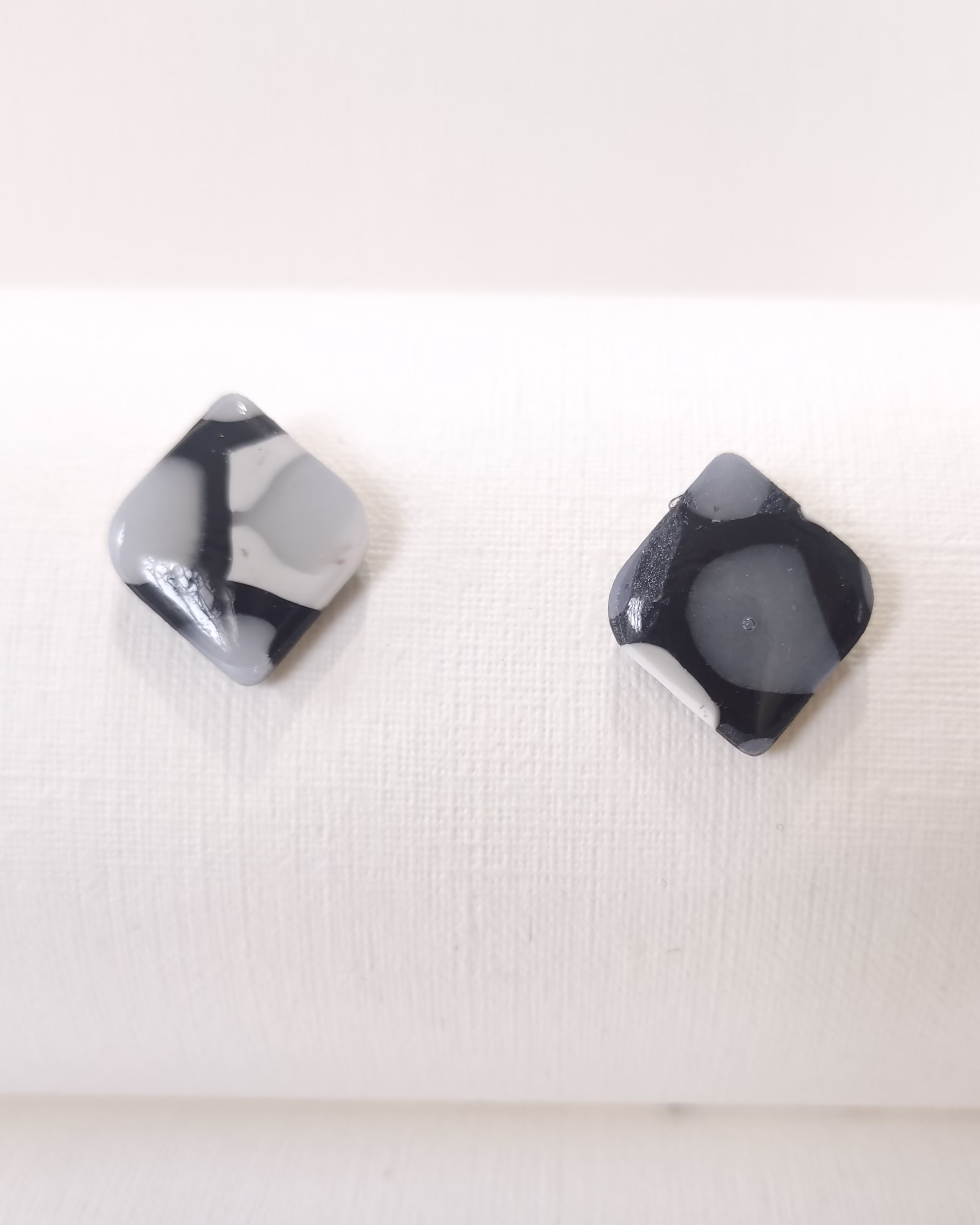 Brincos artesanais em formato quadrado orgânico, em preto e cinza translúcido, acabamento brilhante, feitos à mão.