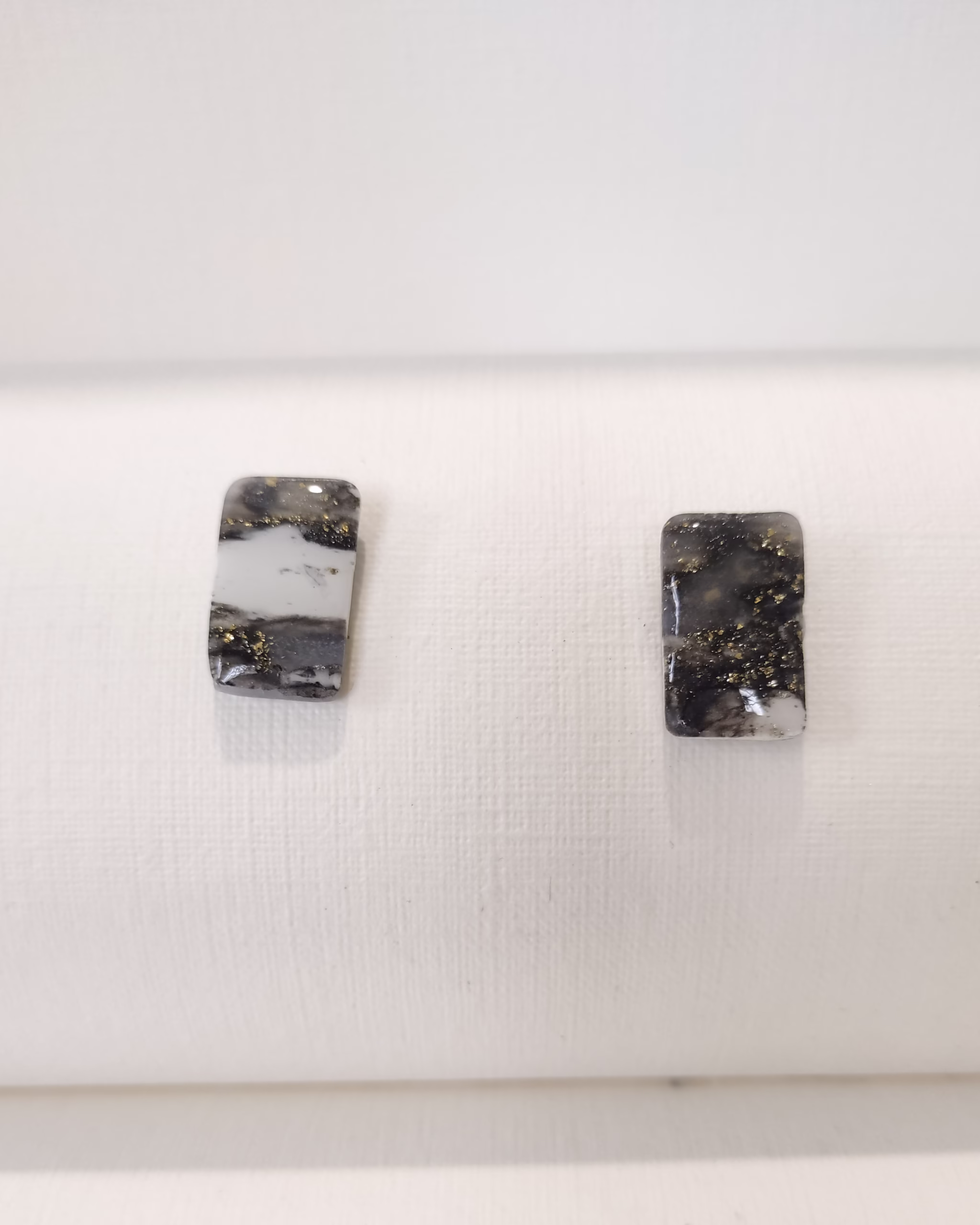 Brincos artesanais retangulares em argila polimérica, com padrão marmoreado preto e branco e detalhes dourados.