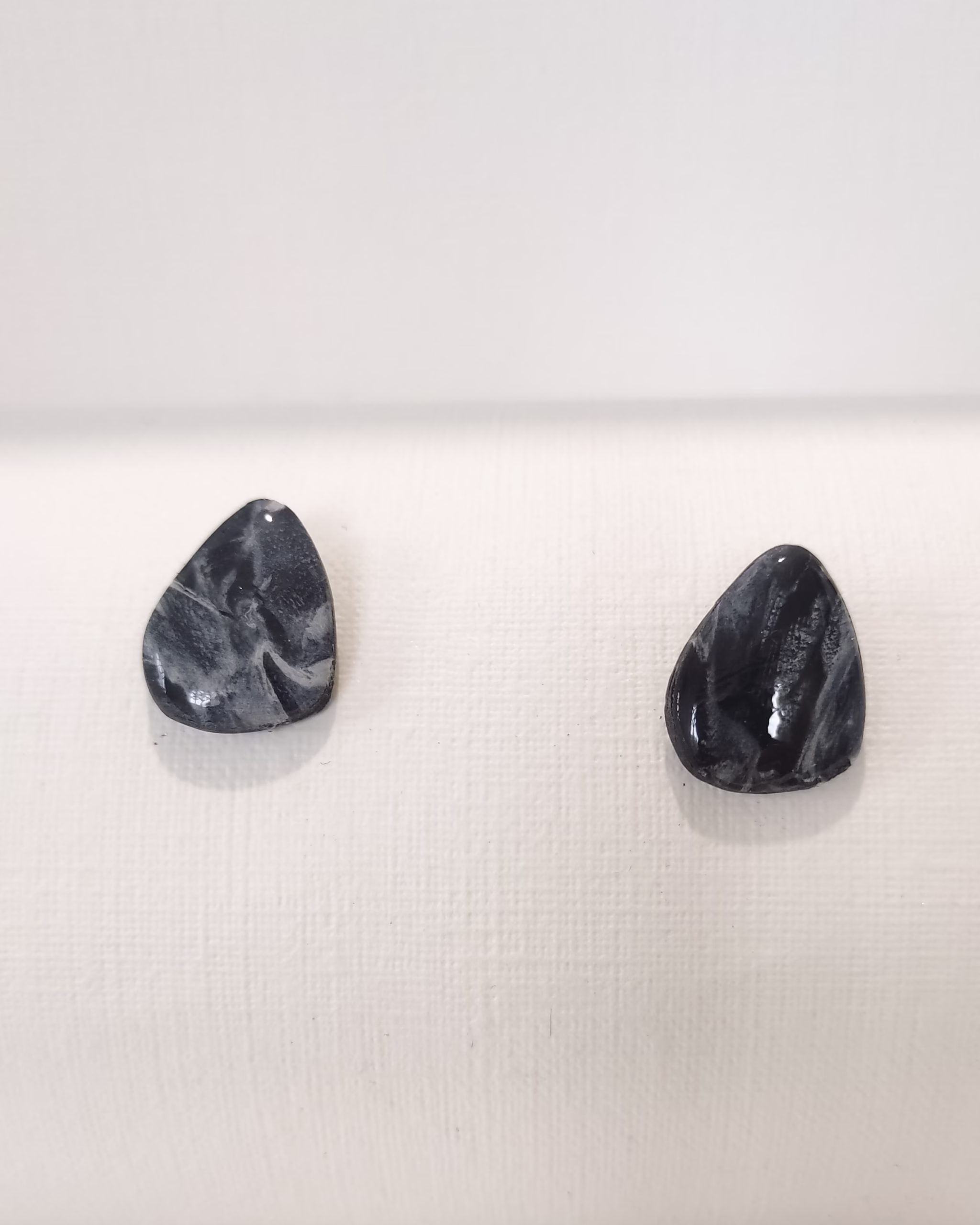 Brincos artesanais em argila polimérica com padrão marmoreado em tons de preto e cinza, formato gota irregular e acabamento brilhante.